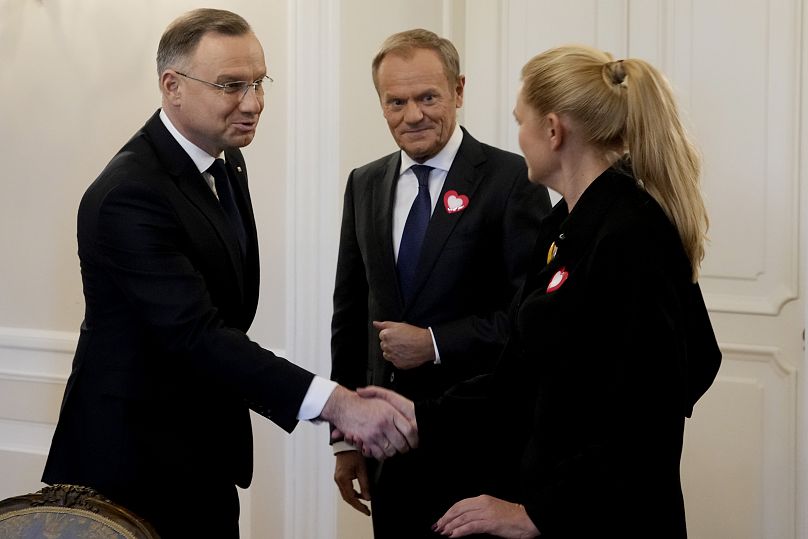 Prezydent Andrzej Duda (z lewej) ściska dłoń członkini opozycji Barbarą Nowacką (z prawej), jak wygląda we wtorek w Warszawie główny lider opozycji Donald Tusk.