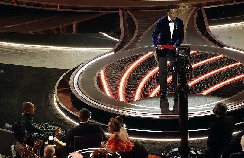 Podczas ceremonii wręczenia Oscarów 2022, która odbędzie się 27 marca, prezenter Chris Rock wkracza na scenę, a Jada Pinkett Smith i Will Smith, którzy później mieli się z nim skonfrontować, obserwują ze swoich miejsc.