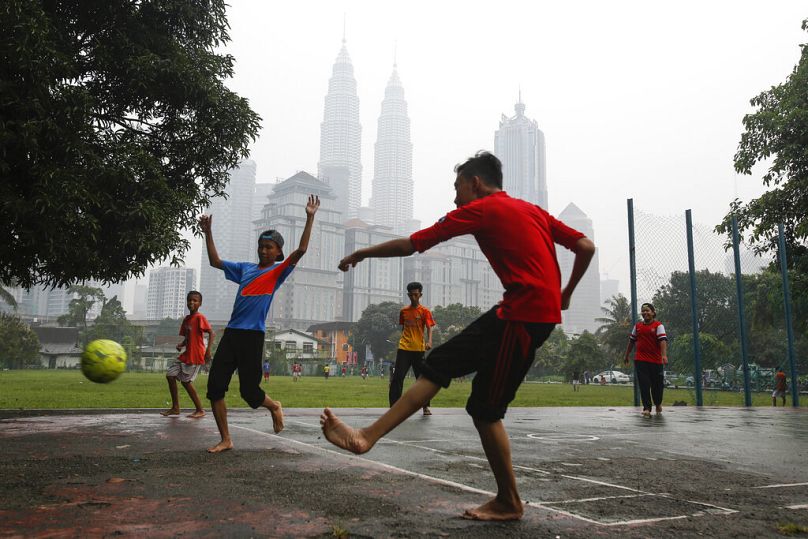 Młody Malezyjczyk gra w piłkę nożną przeciwko charakterystycznemu budynkowi Malezji Petronas Twin Towers w centrum, spowitym mgłą w Kuala Lumpur, wrzesień 2015 r.