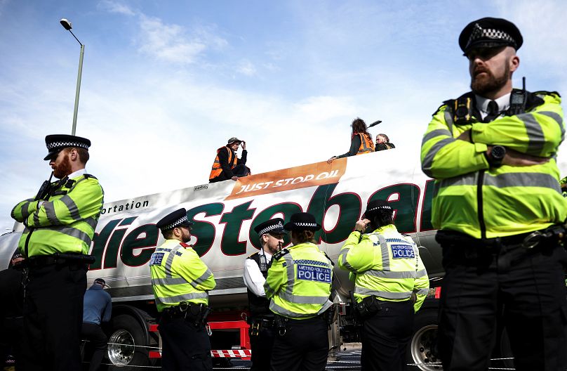 Aktywiści Just Stop Oil siedzą na dachu cysterny z paliwem, podczas gdy policjanci stoją na straży podczas protestu na rondzie w zachodnim Londynie, Wielka Brytania, 14 kwietnia 2022 r.