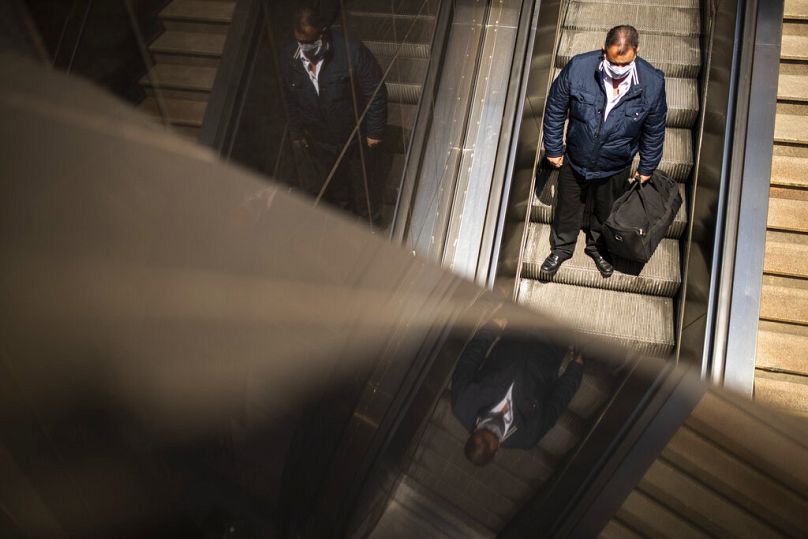 Mężczyzna wjeżdża ruchomymi schodami na stację kolejową i stację metra Schuman w Brukseli, lipiec 2020 r
