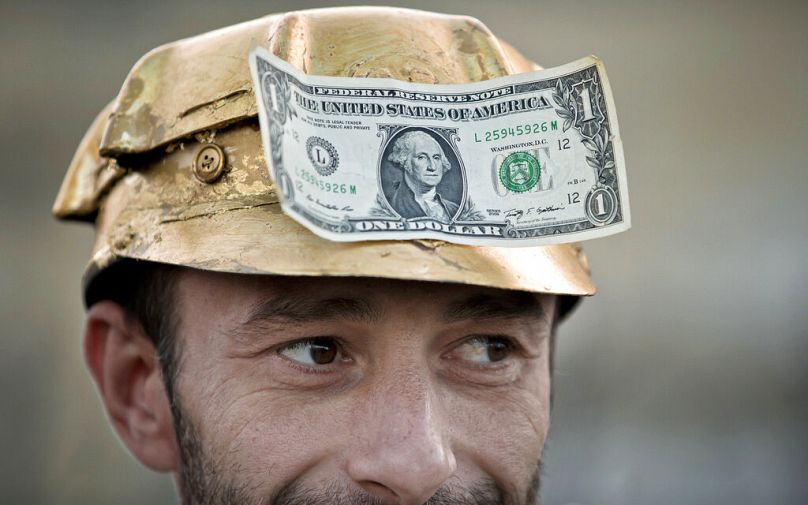 Mężczyzna niesie banknot dolarowy na pomalowanym na złoto hełmie górnika podczas protestu w Bukareszcie, wrzesień 2021 r.