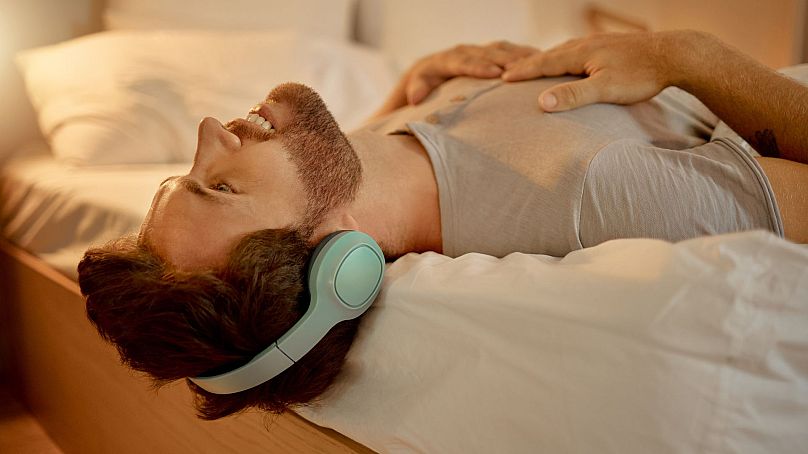 Mężczyzna leżący na łóżku i słuchający muzyki przez słuchawki