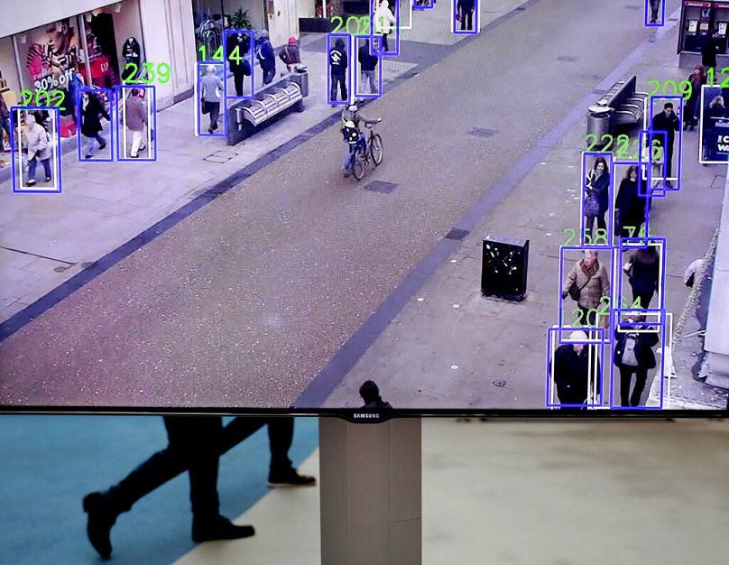 Ludzie chodzą za ekranem przedstawiającym prototyp, który może śledzić ludzi spacerujących ulicą podczas targów technologicznych w Parlamencie Europejskim w Brukseli, październik 2019 r.