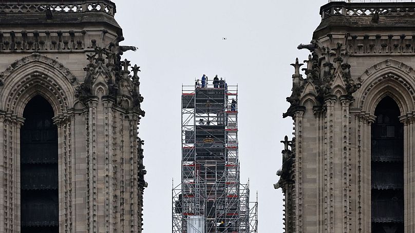 Macron (w środku) odwiedza prace rekonstrukcyjne i krzyż na szczycie nowo odbudowanej iglicy w katedrze Notre-Dame de Paris.