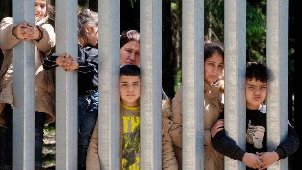 Members of a group of some 30 migrants seeking asylum are seen in Bialowieza, Poland, on Sunday, 28 May 2023 across a wall that Poland has built on its border with Belarus.