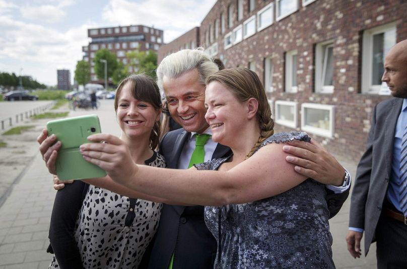 Geert Wilders, przywódca Holenderskiej Partii Wolności, pozuje do selfie z kibicami, podczas gdy jego ochroniarz stoi na straży po oddaniu głosu w Hadze, maj 2014 r.