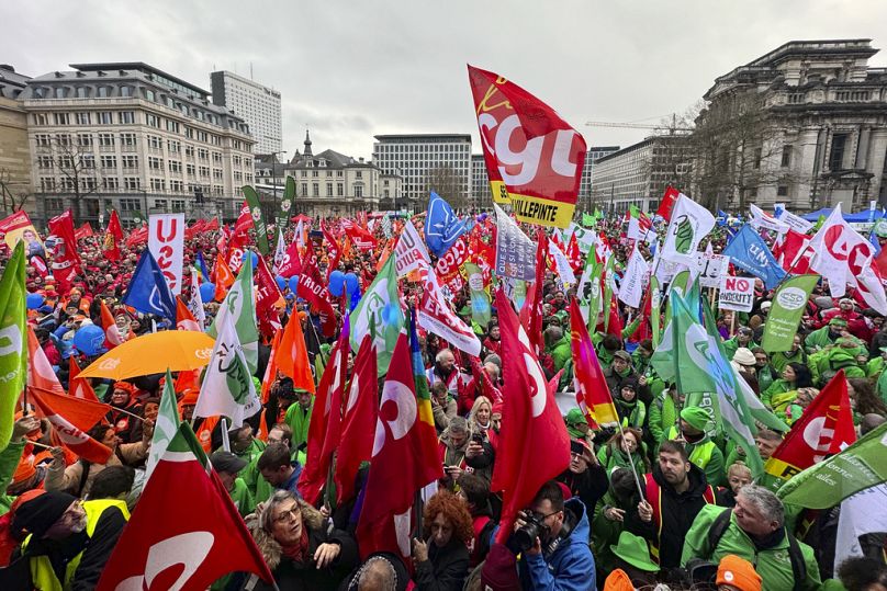 Protestujący trzymają flagi i zbierają się podczas demonstracji przeciwko środkom oszczędnościowym w Brukseli, 12 grudnia 2023 r.