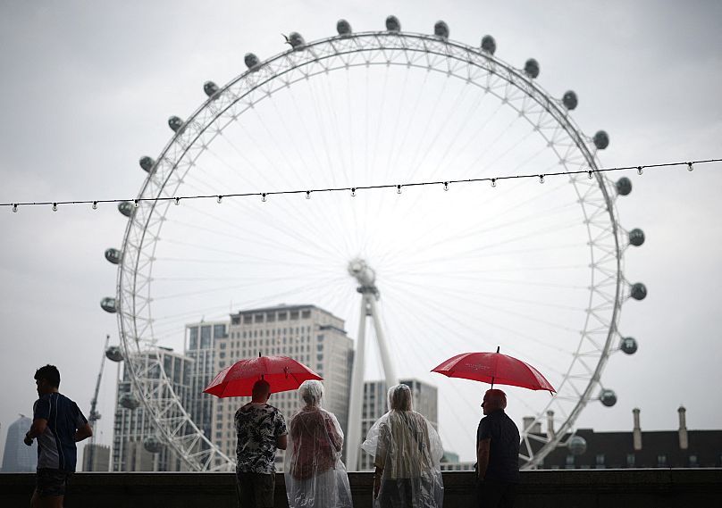 Piesi chronią się przed deszczem pod parasolami, patrząc na charakterystyczny obiekt Londynu, London Eye, z Embankment by the River Thames w centrum Londynu, 18 sierpnia.