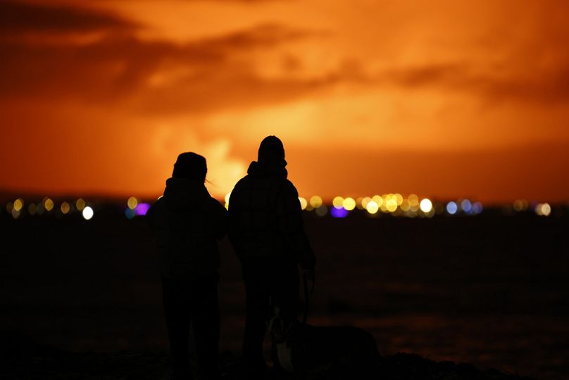 Ludzie obserwują, jak nocne niebo rozświetla się w wyniku erupcji wulkanu na półwyspie Reykjanes w południowo-zachodniej Islandii, widzianej ze stolicy Reykjaviku.