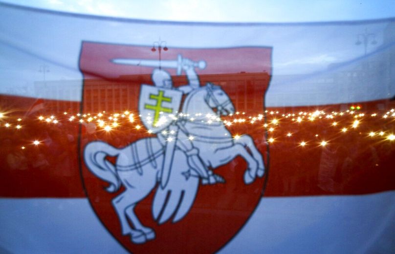 Zwolennicy białoruskiej opozycji widziani przez starą białoruską flagę narodową trzymają telefony podczas gromadzenia się na Placu Niepodległości w Mińsku, sierpień 2020 r.