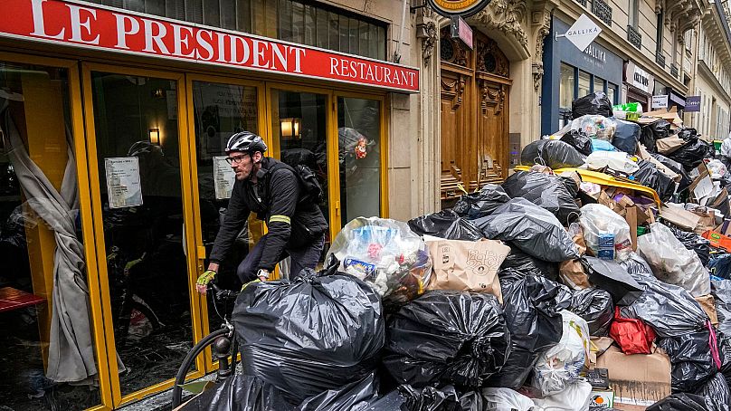 Rowerzysta przejeżdża obok nieodebranego stosu śmieci obok kawiarni w Paryżu, 21 marca 2023 r.