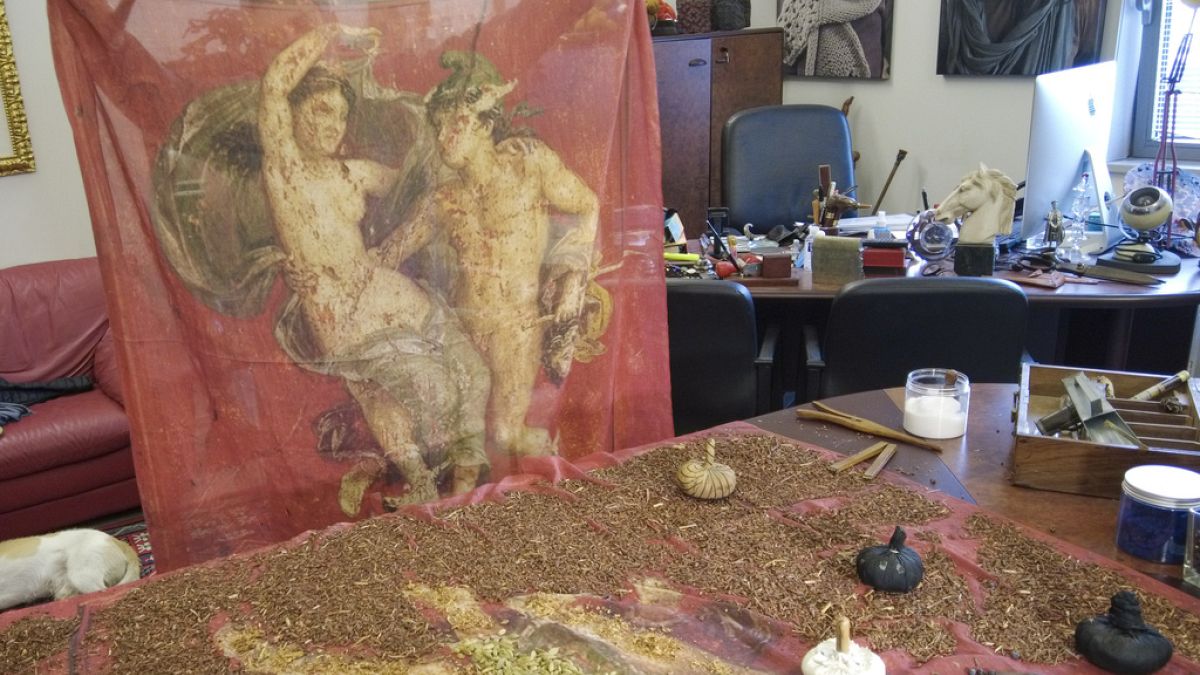 Designer and traditional dyer Claudio Cutuli holds up a finished scarf reproducing an ancient Roman fresco of intertwining Perseus and Andromeda surrounded in a Pompeii red.