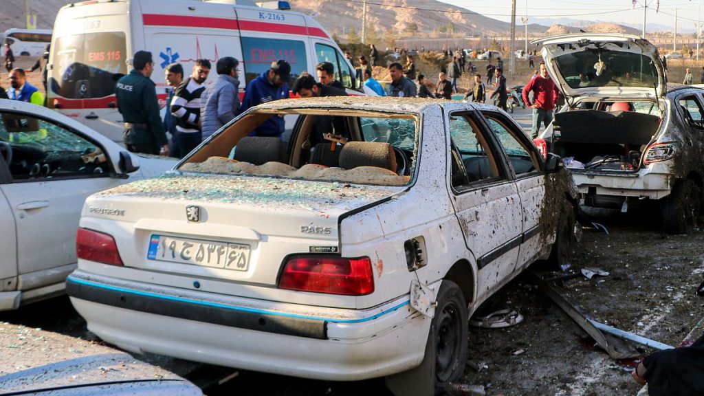 People stay next to destroyed cars after an explosion in Kerman, Iran, Wednesday, Jan. 3, 2024.