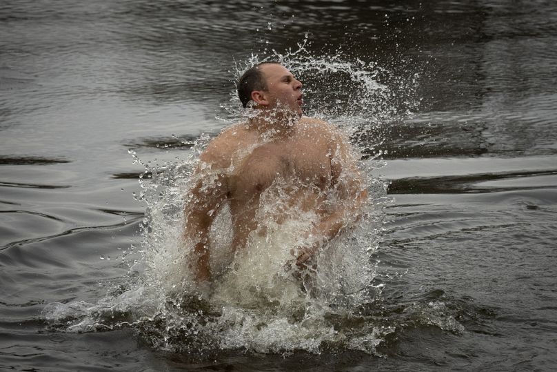 Mężczyzna gestykuluje w lodowatej wodzie Dniepru podczas tradycyjnych obchodów Objawienia Pańskiego w Kijowie na Ukrainie, sobota, 6 stycznia 2024 r.