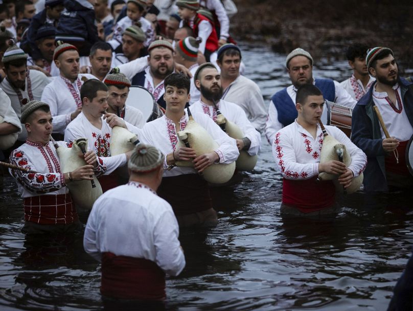 Mężczyźni grają na dudach i bębnach, brodząc do zimnej rzeki Tundzha, aby uczcić Święto Trzech Króli w mieście Kalofer w Bułgarii.