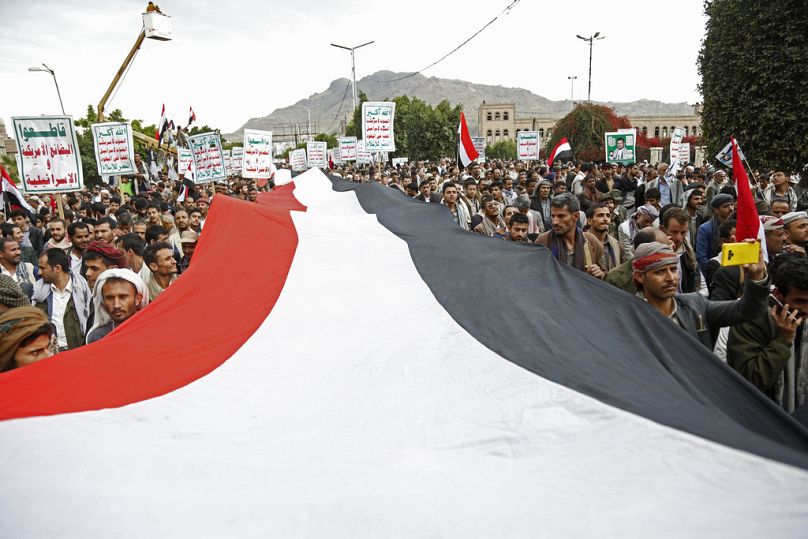 Zwolennicy Houthi skandują hasła, trzymając tabliczki z odczytem 