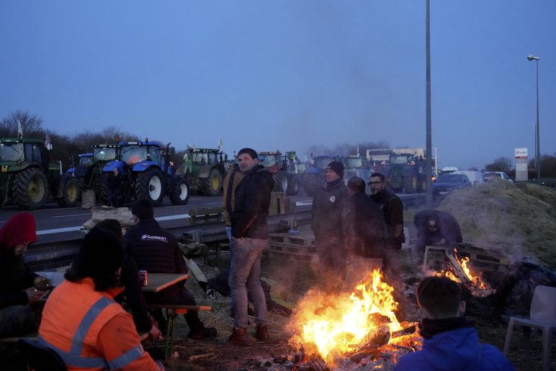 Rolnicy rozgrzewają się przy ognisku, blokując traktorami autostradę w Ourdy na południe od Paryża, w środę