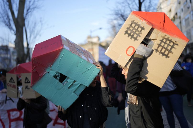 Demonstranci noszą na głowach domy z tektury podczas protestu przeciwko kryzysowi mieszkaniowemu w Portugalii, Lizbona, styczeń 2024 r.