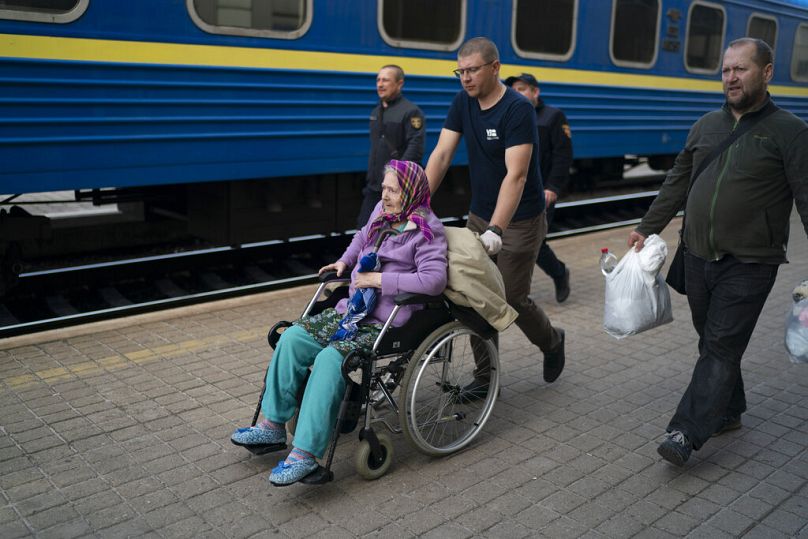 Wolontariusze pomagają starszej kobiecie wsiąść do pociągu uciekającego przed wojną w Siewierodoniecku i pobliskich miejscowościach na stacji kolejowej w Pokrowsku, kwiecień 2022 r.