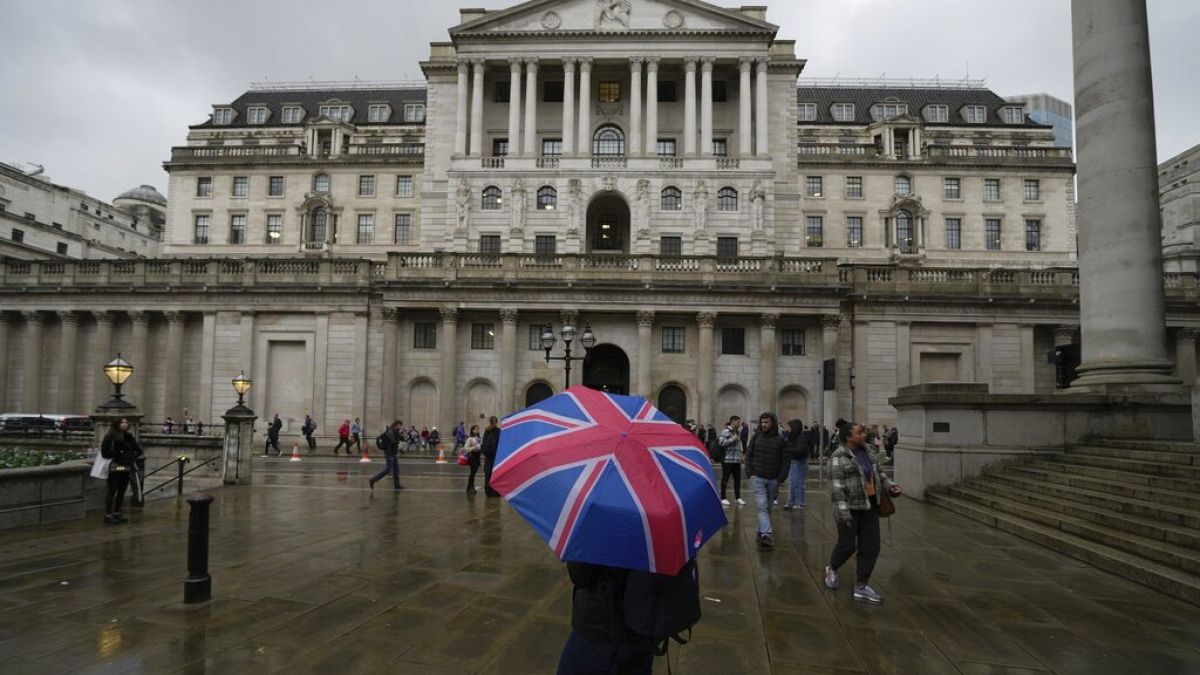 A woman with an umbrella stands in front of the Bank of England, at the financial district in London, Thursday, Nov. 3, 2022.