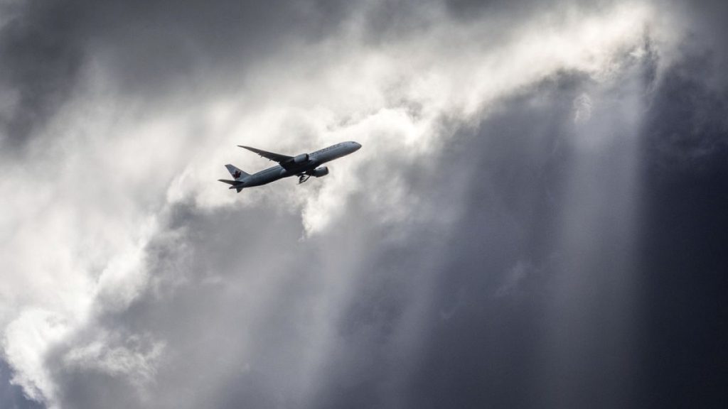 An Air Canada plane flies underneath dark clouds illuminated by some sun rays above Frankfurt, Germany, Thursday, March 2, 2017.