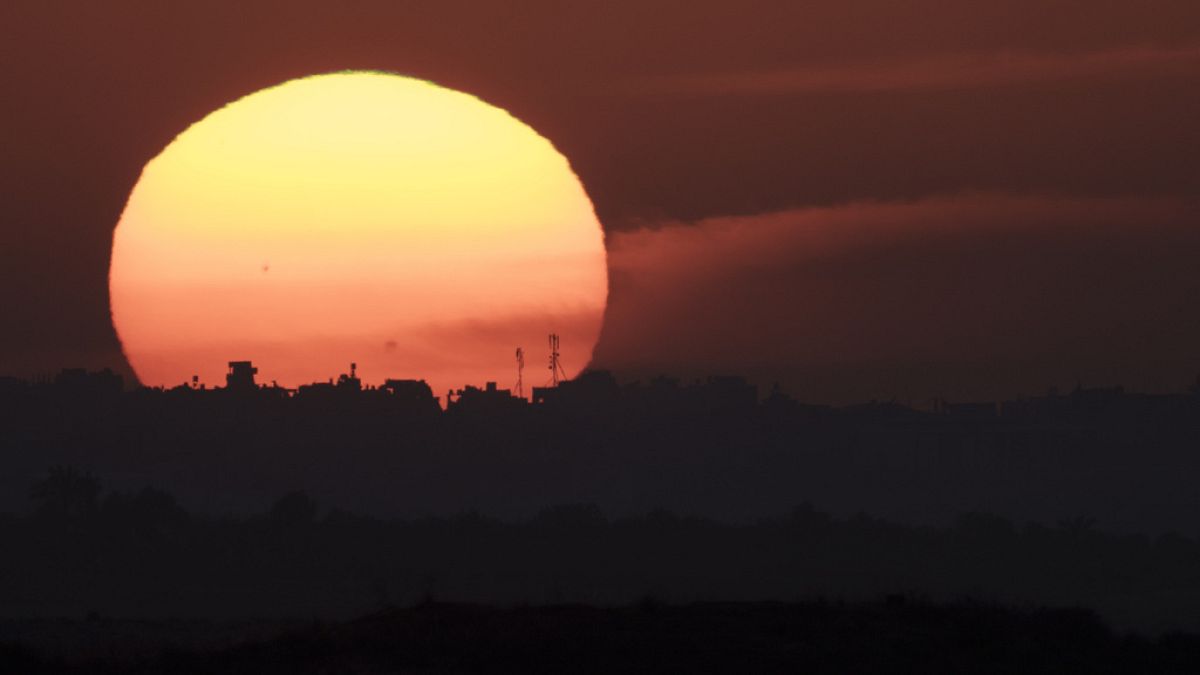 The sun sets behind the buildings in the Gaza Strip as seen from southern Israel, Tuesday, Jan. 16, 2024.