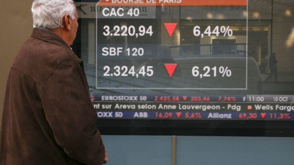 A passer-by stops to view a screen displaying markets news, with Paris