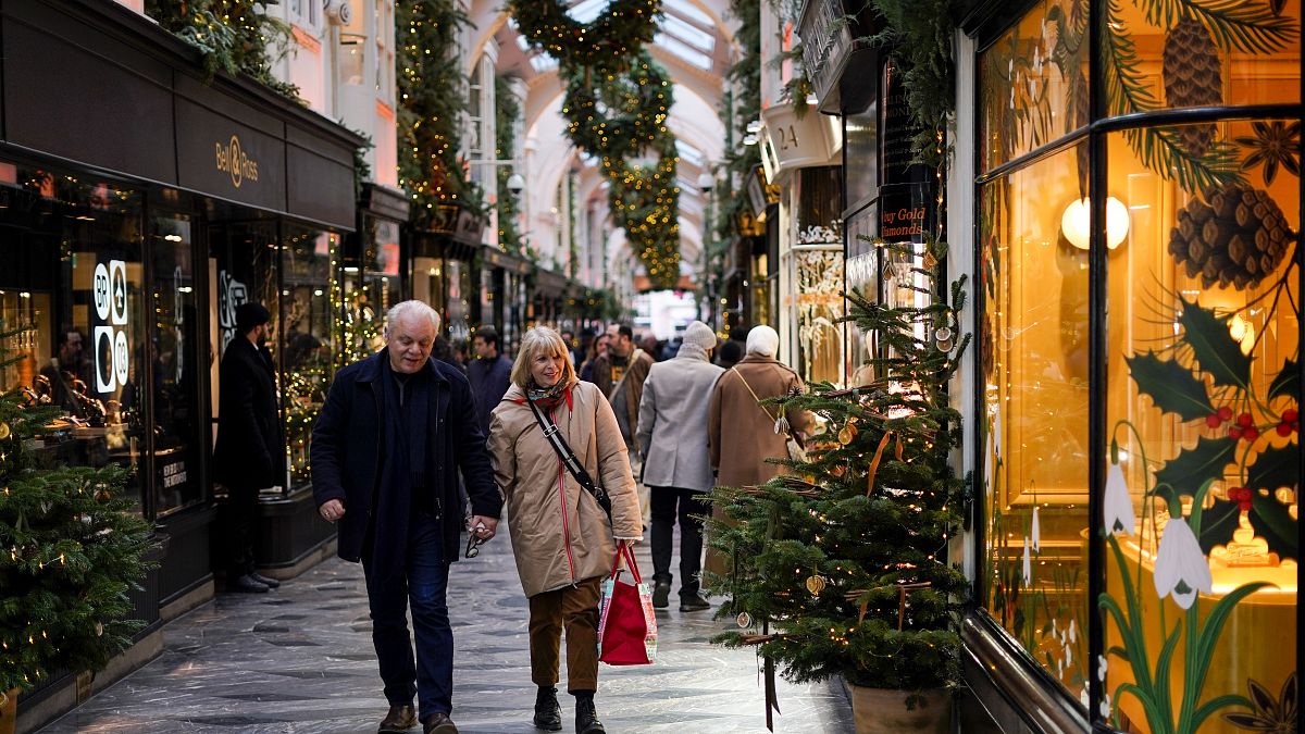 People hold hands as they walk in a Christmas decorated Burlington Arcade, in London, 2023.