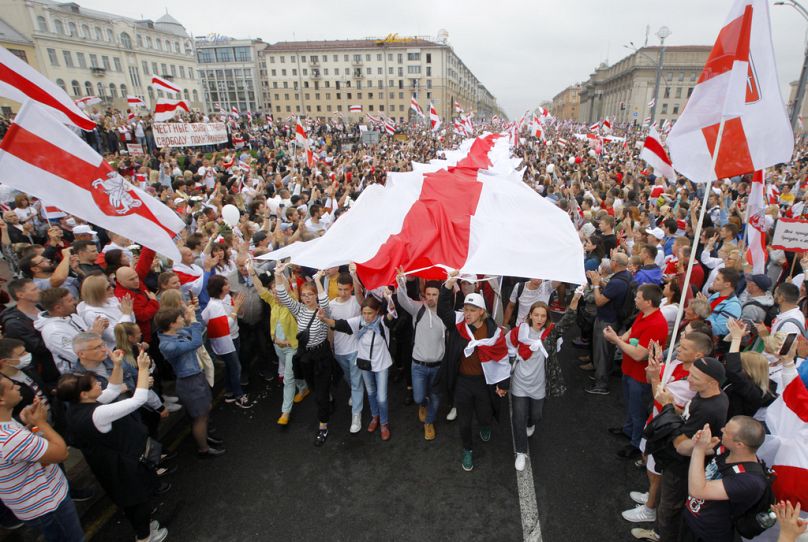 Demonstranci niosą ogromną historyczną flagę Białorusi, a tysiące zbierają się na proteście na placu Niepodległości w Mińsku, 2020.