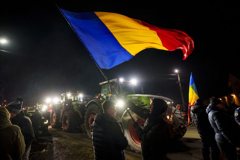 Mężczyzna macha flagą obok szeregu traktorów blokujących pierwszy pas drogi prowadzącej do Bukaresztu, w Afumati w Rumunii, poniedziałek, 15 stycznia 2024 r.