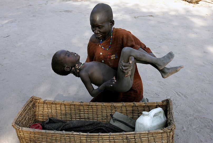 Matka delikatnie umieszcza syna w koszyku, zabierając go do kliniki Medecins Sans Frontieres po tym, jak zachorował na malarię, w Lankien w południowym Sudanie, 2005.