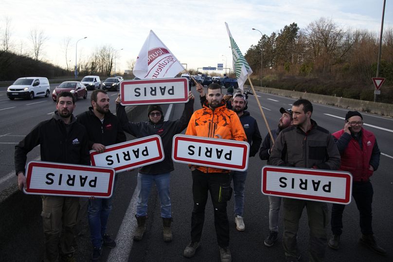 Rolnicy trzymają do góry nogami znaki drogowe Paryża na zablokowanej autostradzie, środa, 31 stycznia 2024 r. w Chilly-Mazarin, na południe od Paryża.