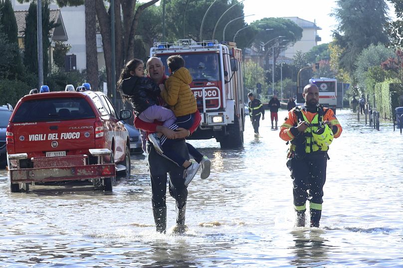 Mężczyzna niesie dzieci przez wodę powodziową. Służby ratunkowe są na miejscu po ulewnych opadach deszczu, Toskania we Włoszech, listopad 2023 r.