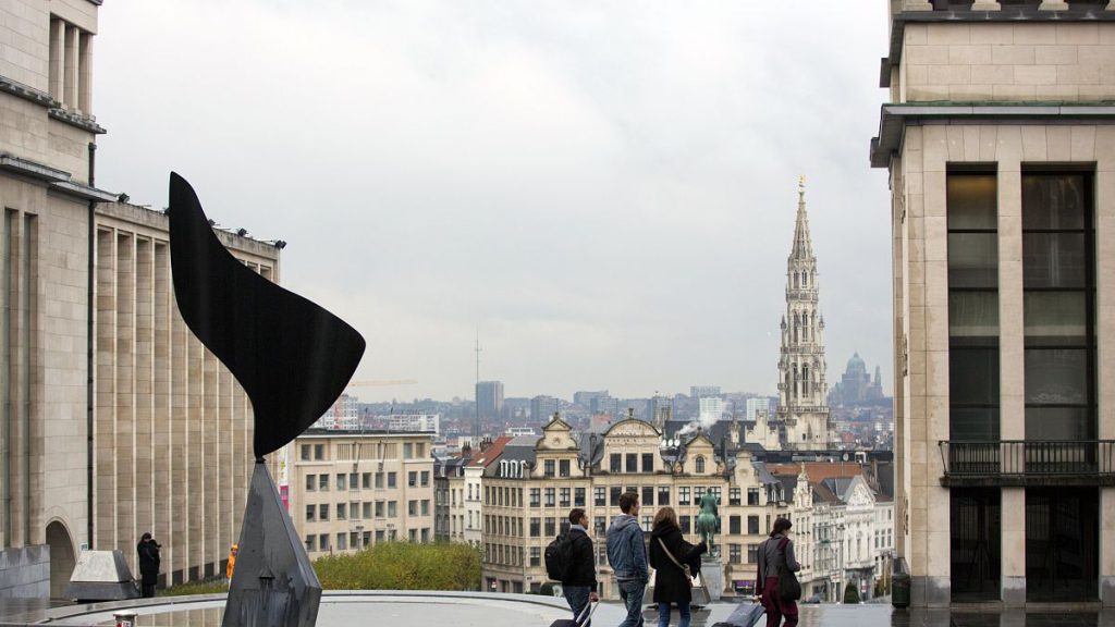 People walk with luggage with the city of Brussels as a backdrop