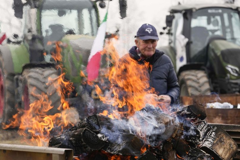 Rolnik siedzi przy ognisku podczas zgromadzenia w pobliżu skrzyżowania autostrad w Melegnano pod Mediolanem, luty 2024 r.