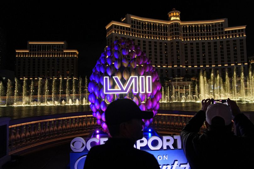 Ludzie stoją przy oznakowaniu Super Bowl, gdy fontanny Bellagio wybuchają wzdłuż Las Vegas Strip przed Super Bowl