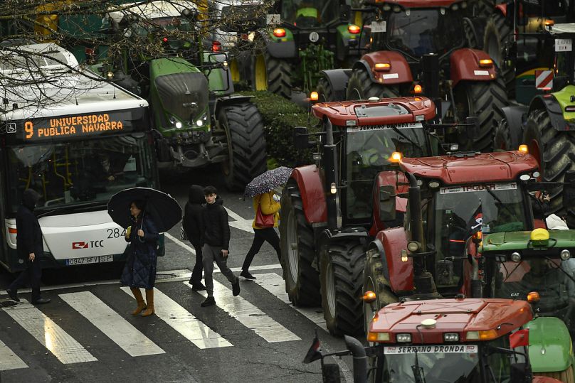 Pieszy przechodzi przez ulicę, gdy rolnicy z traktorami maszerują przez centrum miasta, biorąc udział w proteście, w Pampelunie, luty 2024 r.
