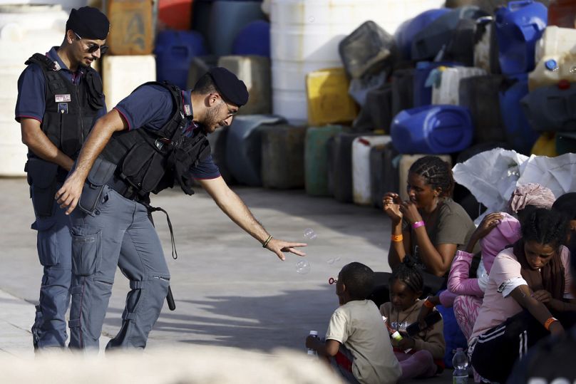 Policjant bawi się z dzieckiem-migrantem dmuchającym bańki mydlane w porcie na sycylijskiej wyspie Lampedusa, listopad 2023 r.