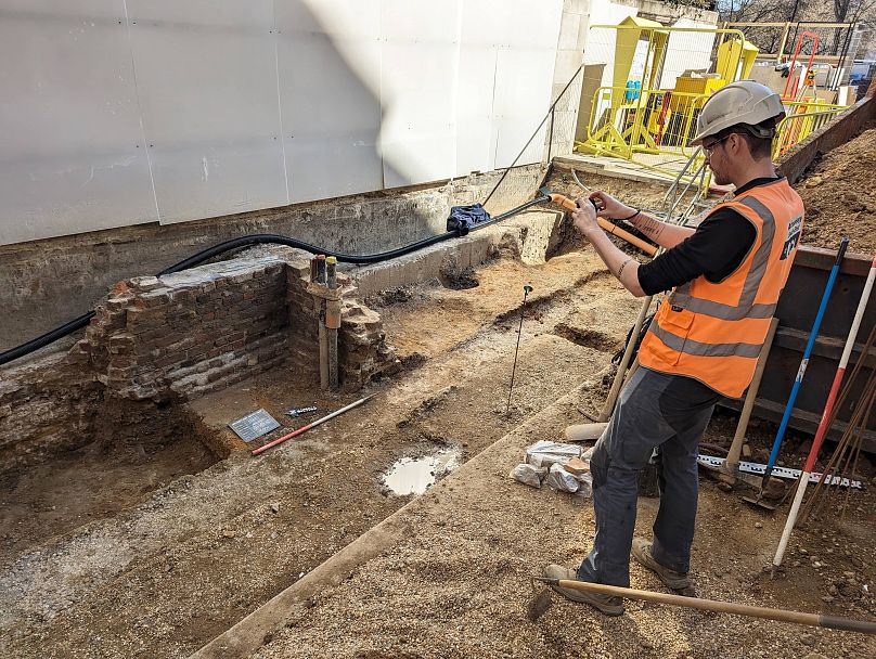 Archeolog fotografuje część wykopalisk, w tym fragment pośredniowiecznego muru.