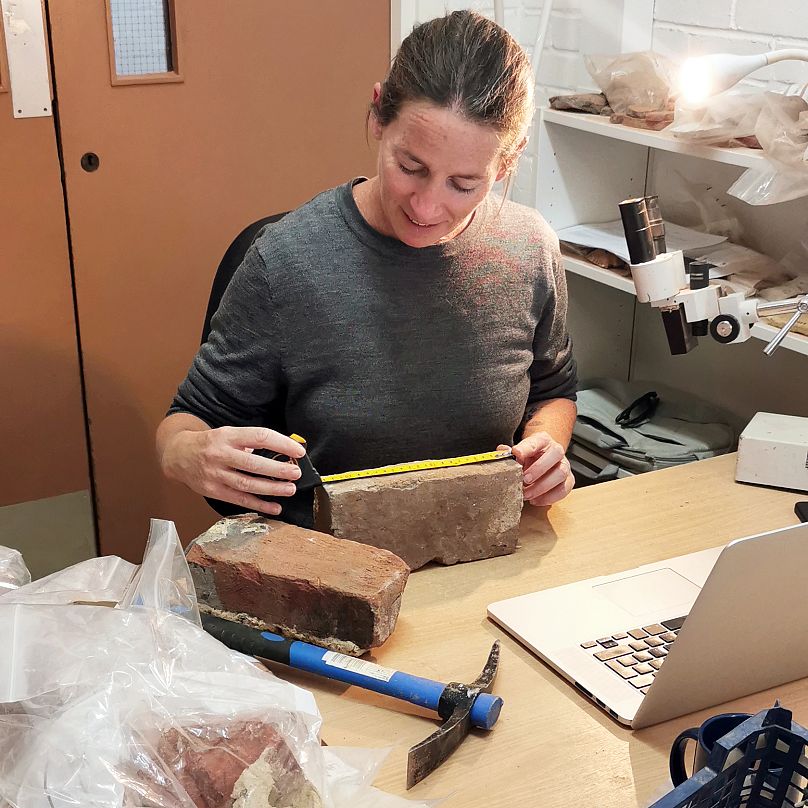 Rae Regensberg, specjalistka ds. ceramicznych materiałów budowlanych w południowo-wschodniej archeologii, przygląda się ceglem z wykopalisk.