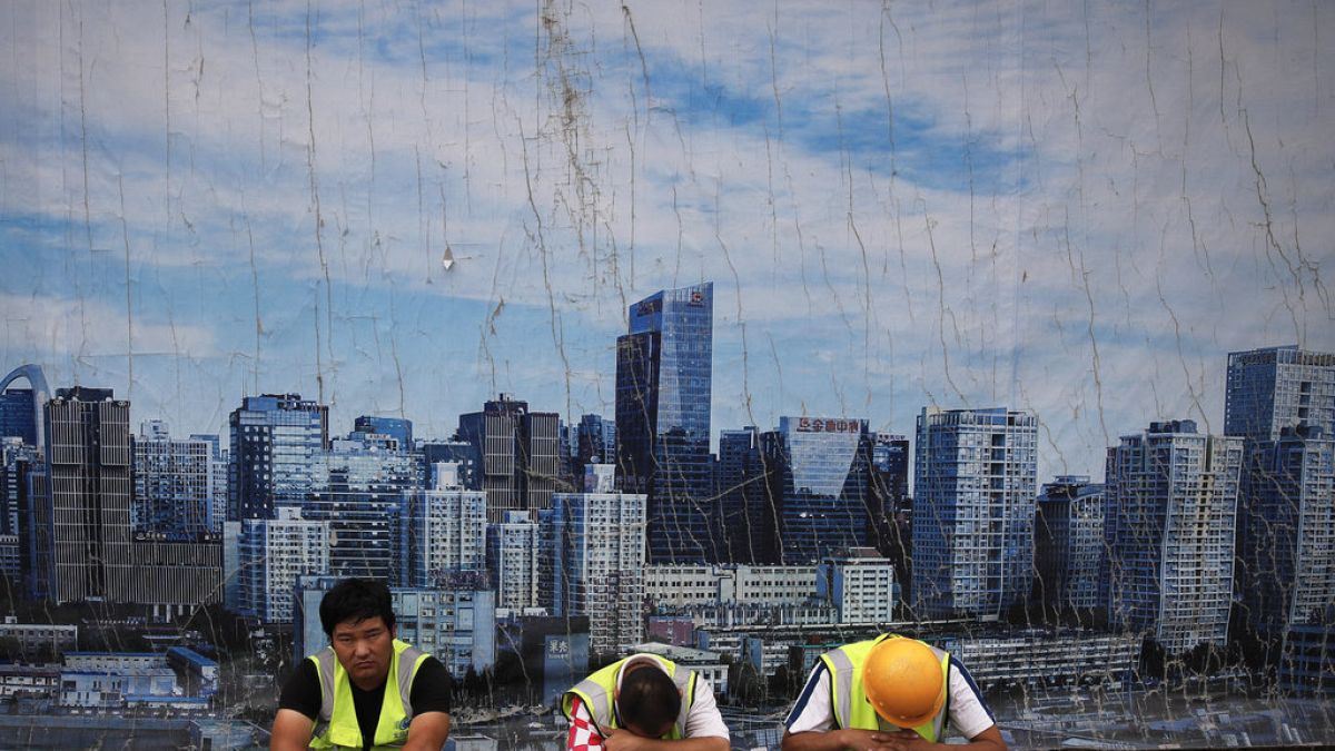 Chinese workers take a break outside a construction site wall depicting the skyline of the Chinese capital at the Central Business District in Beijing, Tuesday, June 26, 2018.