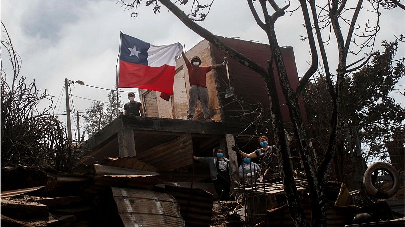 Mieszkaniec pozuje z chilijską flagą spalonego domu po tym, jak pożary lasów dotarły do ​​jego okolicy w Vina del Mar w Chile, niedziela, 4 lutego 2024 r.