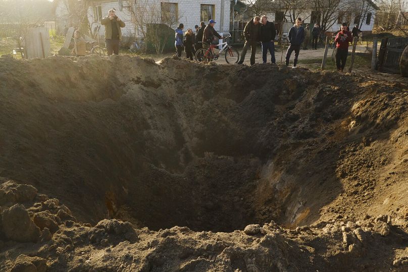 Ludzie patrzą na krater po eksplozji we wsi Horodnia, obwód czernihowski, kwiecień 2022 r.