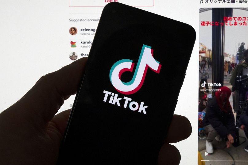 Logo TikTok widać na telefonie komórkowym przed ekranem komputera, na którym wyświetlany jest ekran główny TikTok, sobota, 18 marca 2023 r., w Bostonie.