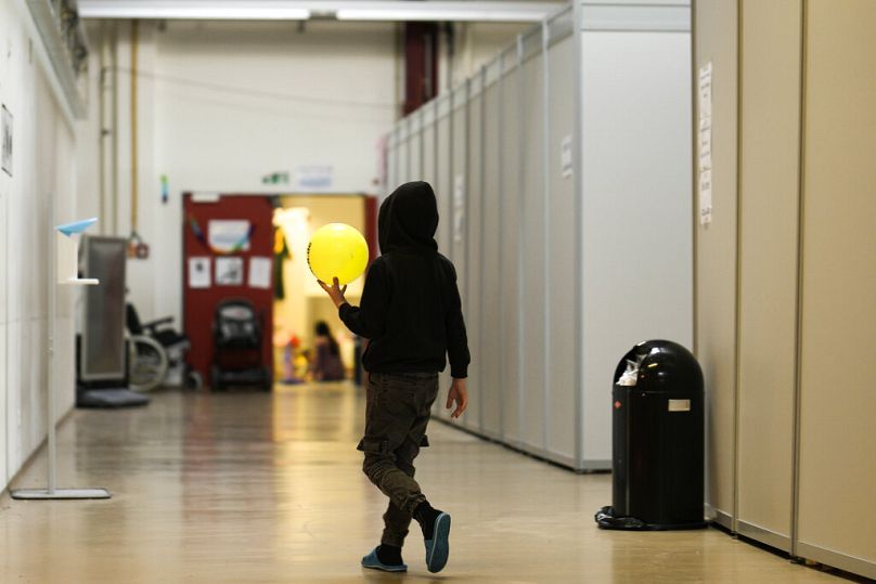 Chłopiec z piłką spaceruje obok prowizorycznych miejsc do spania w tymczasowym schronisku dla uchodźców na byłym lotnisku Tegel w Berlinie, Niemcy, 9 listopada 2022 r.