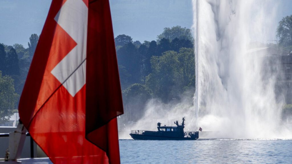 A police boat passes by a Swiss flag and a fountain on the Lake Geneva in Geneva, Switzerland Tuesday, June 15, 2021.
