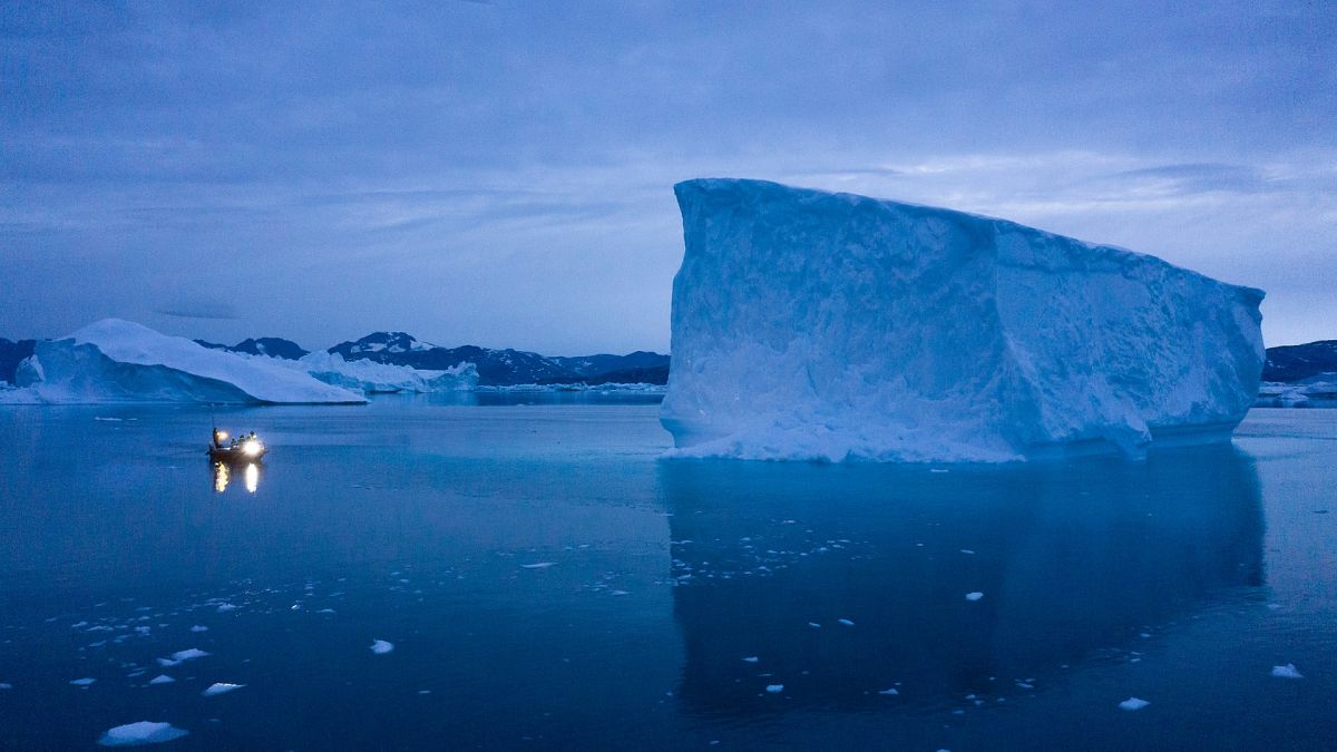 A boat navigates at night next to large icebergs in eastern Greenland.