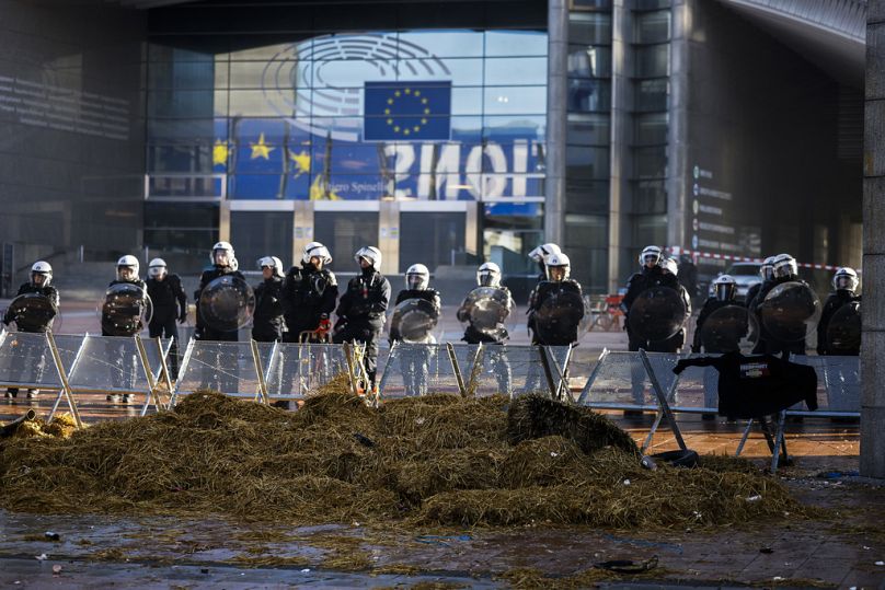 Funkcjonariusze policji walczący z zamieszkami stoją na straży w zamkniętej strefie bezpieczeństwa przed Parlamentem Europejskim podczas protestu rolników podczas spotkania europejskich przywódców na szczycie UE