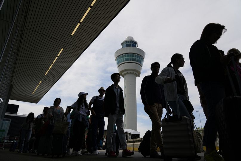 Na tym zdjęciu do pliku podróżni czekają przed budynkiem terminala, aby odprawić się i wejść na pokład samolotu na lotnisku Schiphol w Holandii